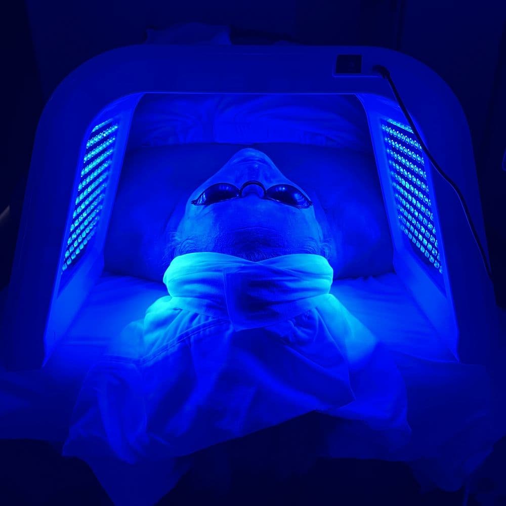 A client resting under an LED light panel in a dim treatment room