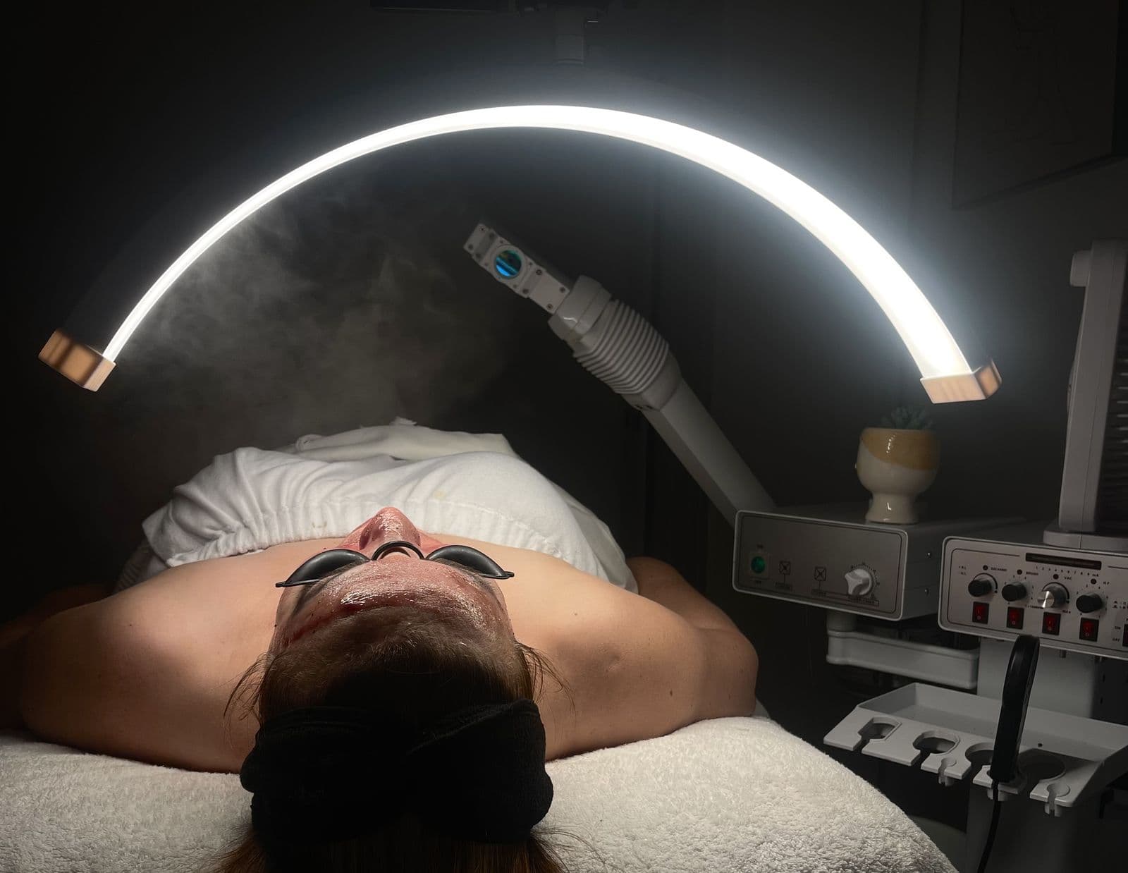 A client lying back under a glowing arc light while a steamer warms the skin