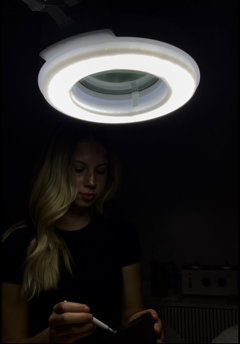 Esthetician working under a lash lamp in a dim studio