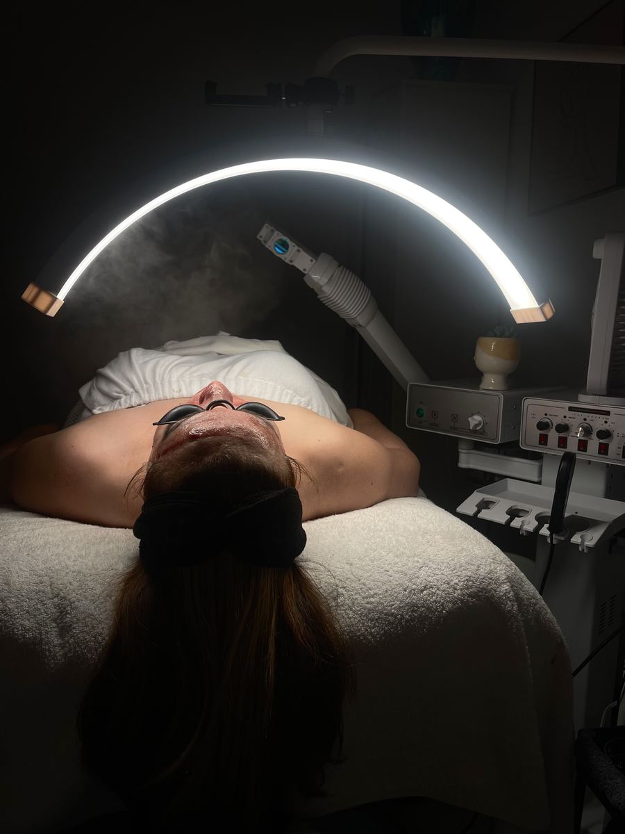 Client resting under a facial steamer and a glowing arc light